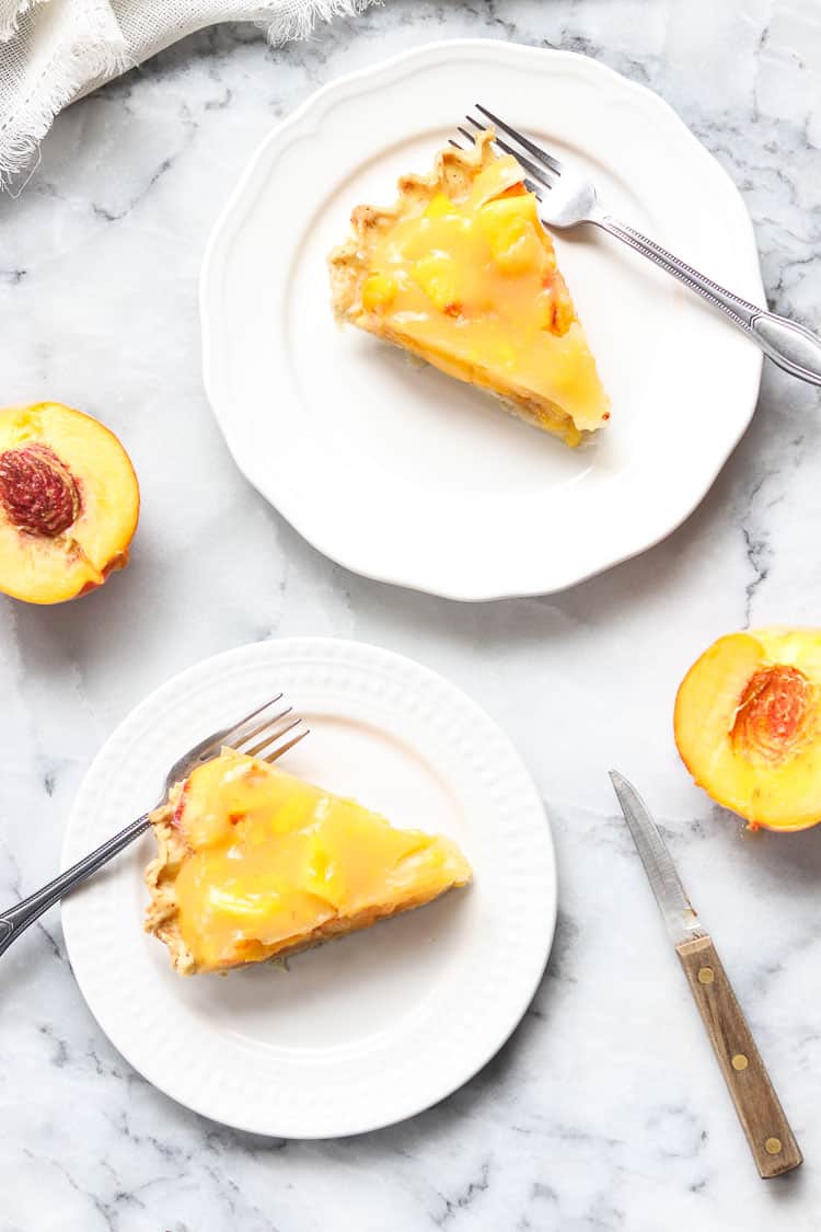 wide overhead shot of fresh peach pie slices on plates with fresh cut peach beside on marble background