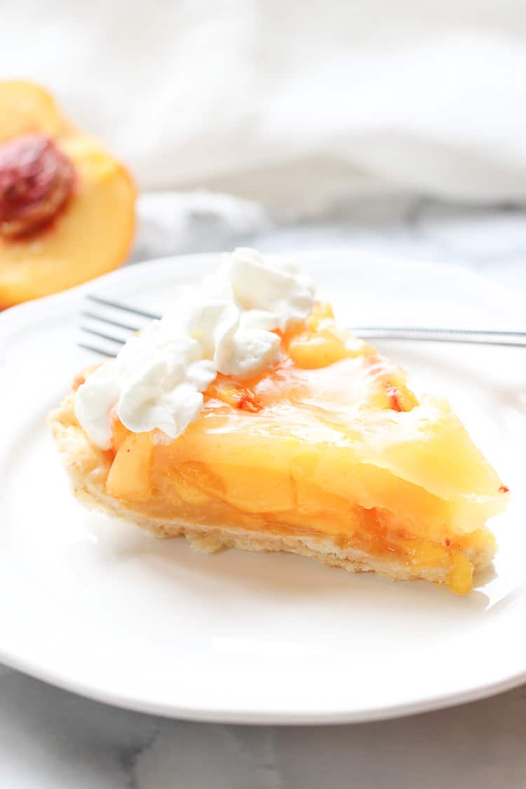 side overhead shot of a slice of fresh peach pie on a white plate with vegan whip cream topping