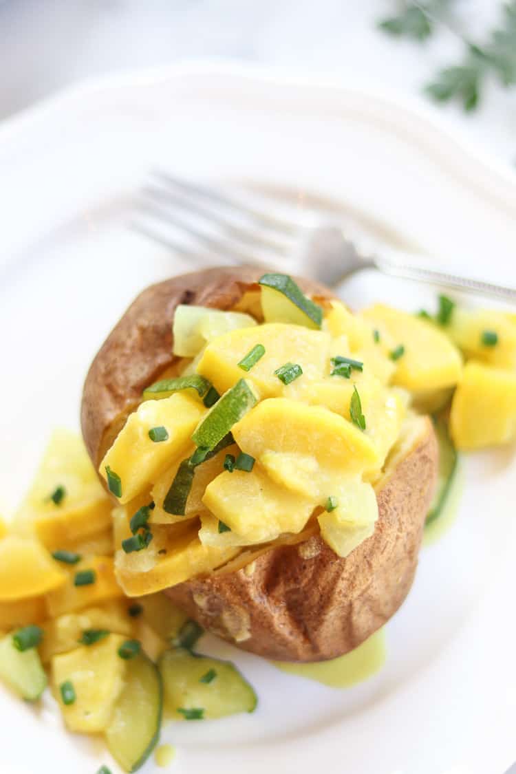 yellow and zucchini squash served over a baked potato on a white plate