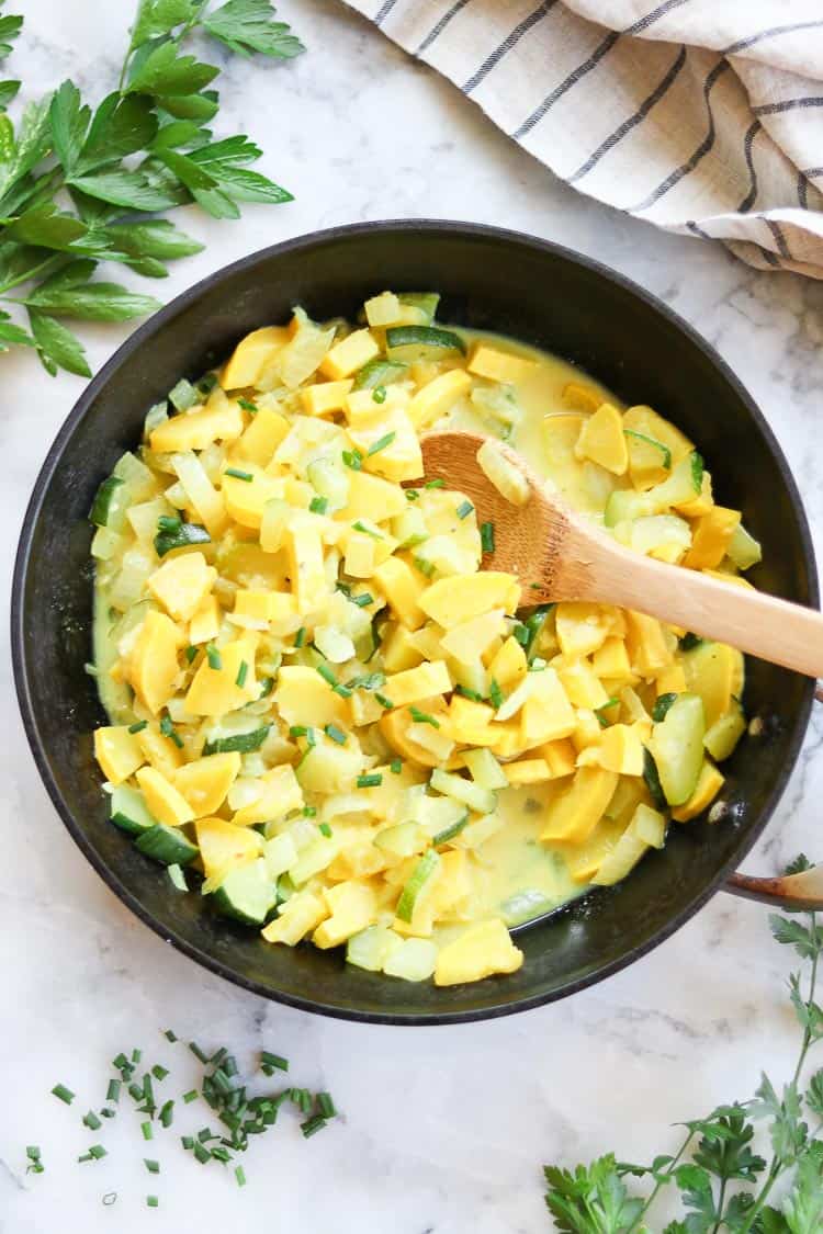 overhead shot of cooked squash in a black skillet with wooden spoon 