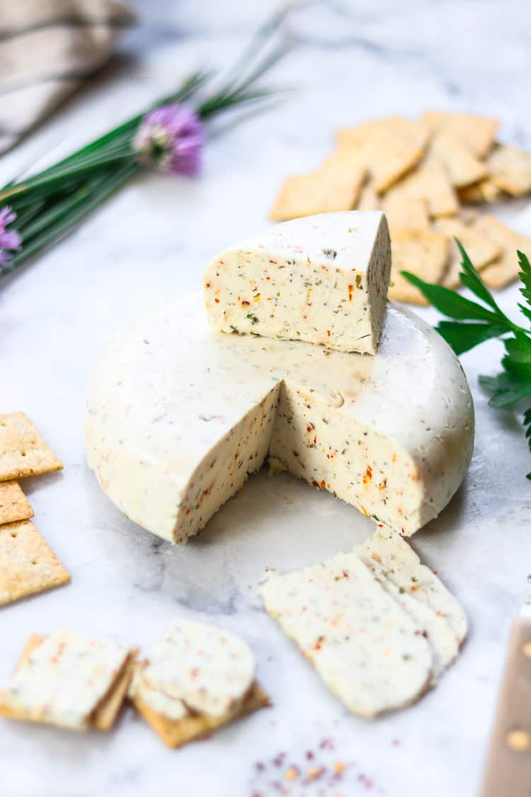 side overhead shot of vegan cheese wheel with a chunk and some slices cut out and placed on crackers