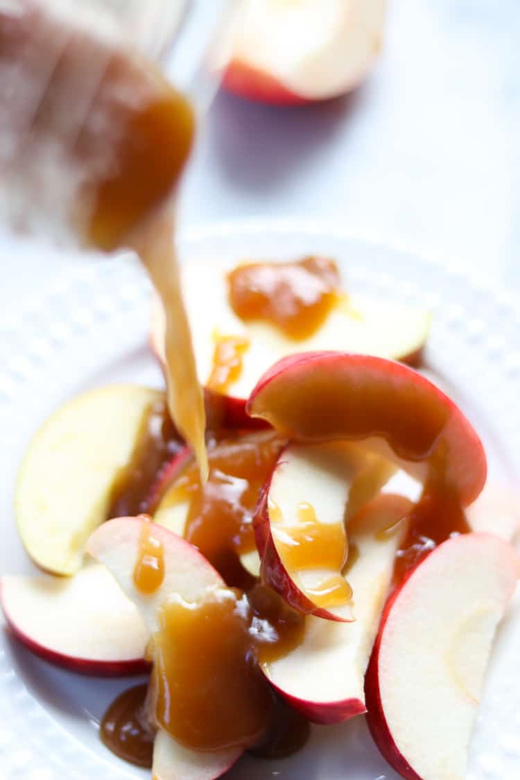 side overhead shot of vegan caramel being poured from a jar onto sliced apples on a white plate