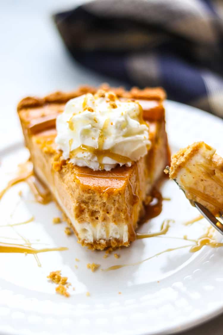 side closeup shot of vegan cheesecake showing the layers on the end with a forkful removed and topped with caramel sauce and vegan whip cream