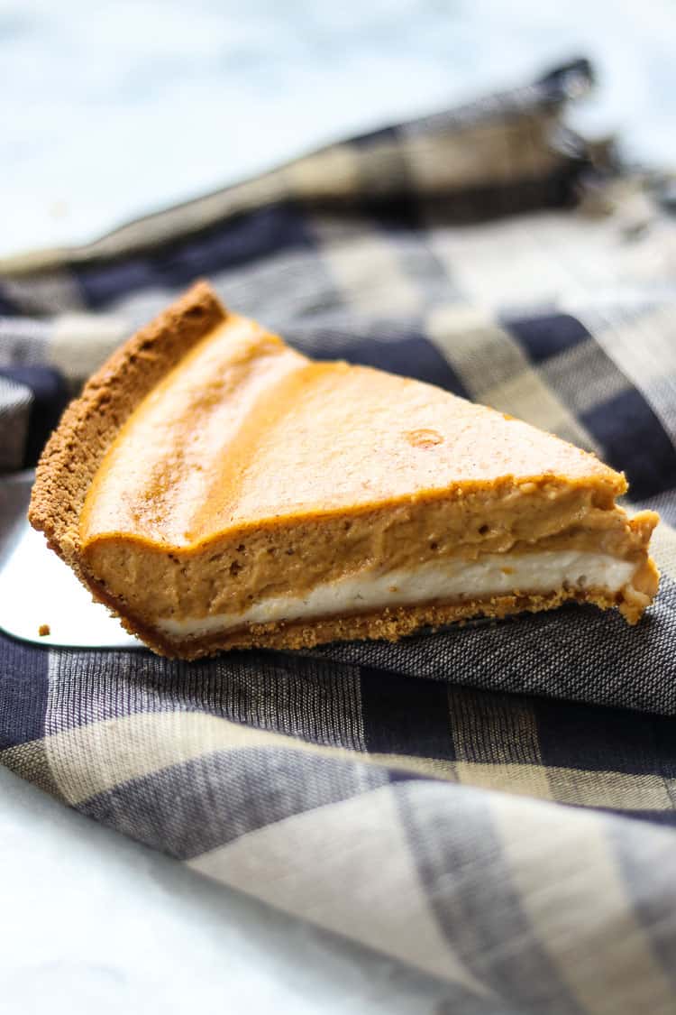 side shot of vegan double layer pumpkin cheesecake on a silver server over a plaid napkin