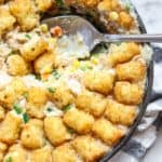 overhead closeup shot of vegan tater tot casserole in a iron skillet with a spoonful taken out