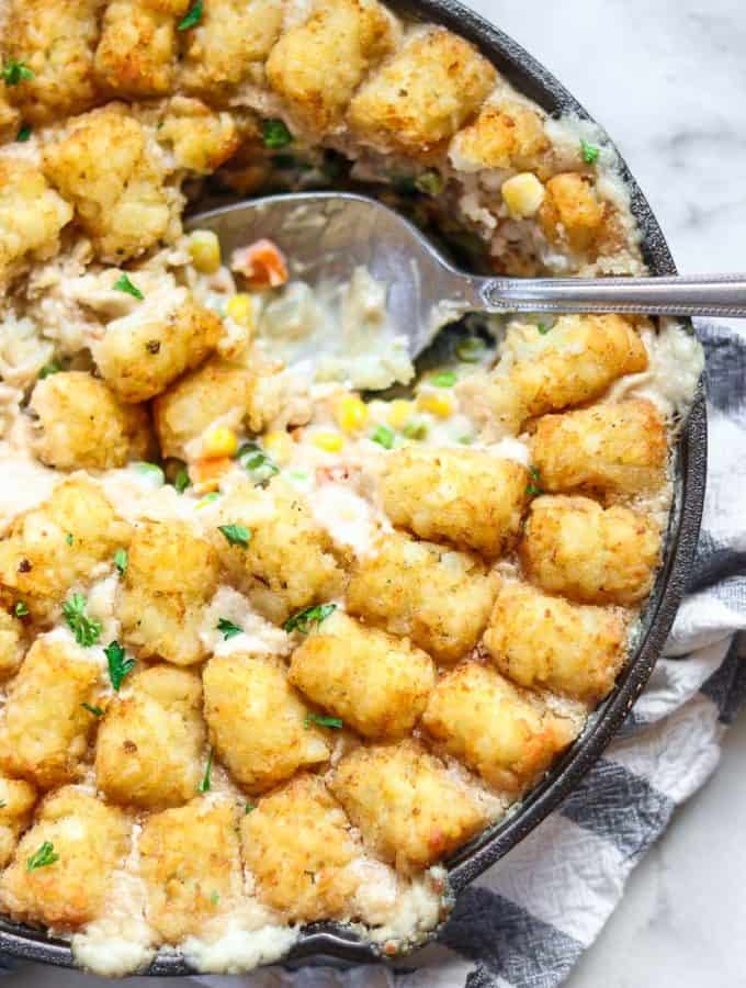 overhead closeup shot of vegan tater tot casserole in a iron skillet with a spoonful taken out