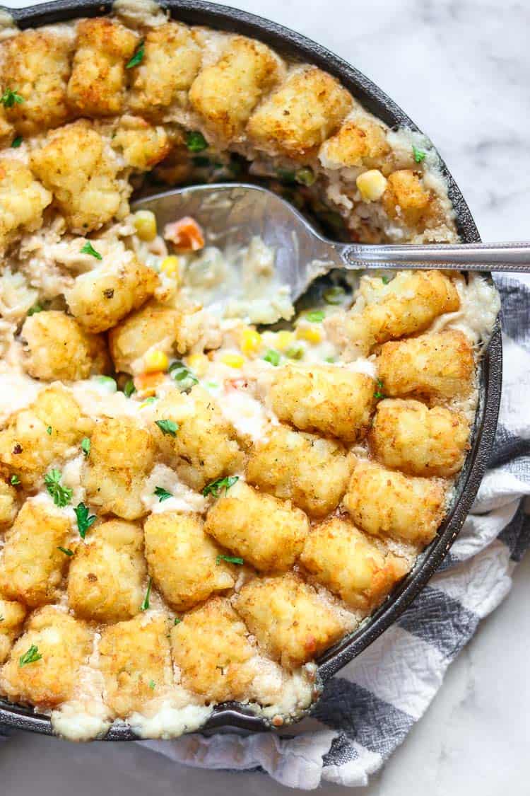 overhead closeup shot of vegan tater tot casserole in a iron skillet with a spoonful taken out