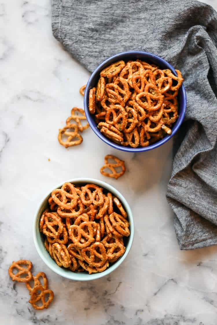 wide overhead photo of two separate ceramic bowl filled with seasoned pretzels sitting on a marble surface