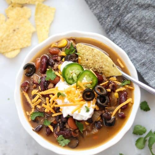 overhead photo of vegan taco soup in white bowl with a variety of vegan garnishes including vegan sour cream and cheese