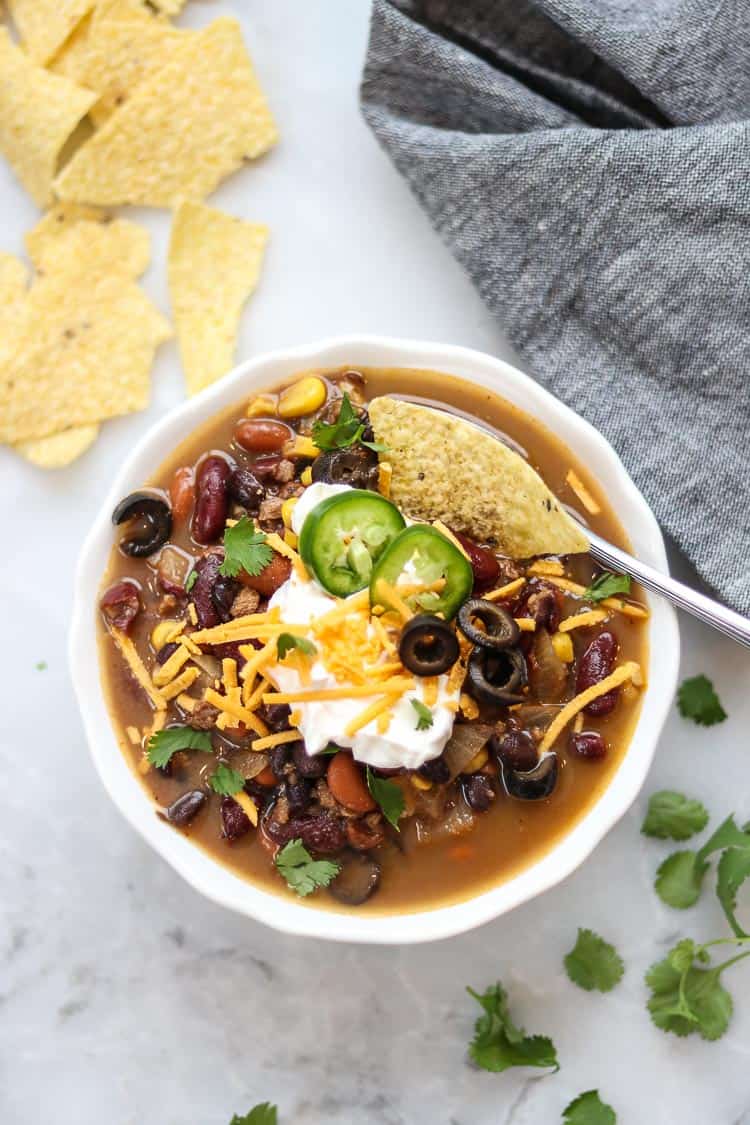 overhead photo of vegan taco soup in a white bowl with vegan cheese, sour cream, and sliced chilis on top