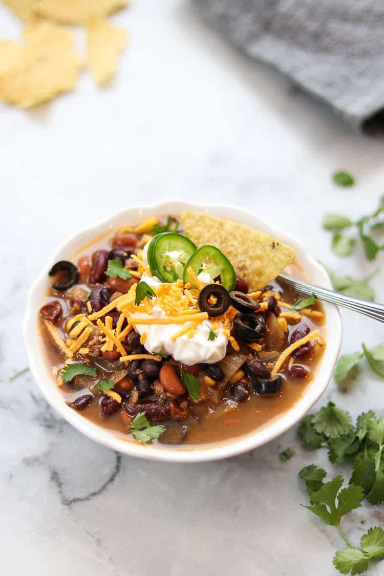 side closeup shot of vegan taco soup in a white bowl on a white marble background