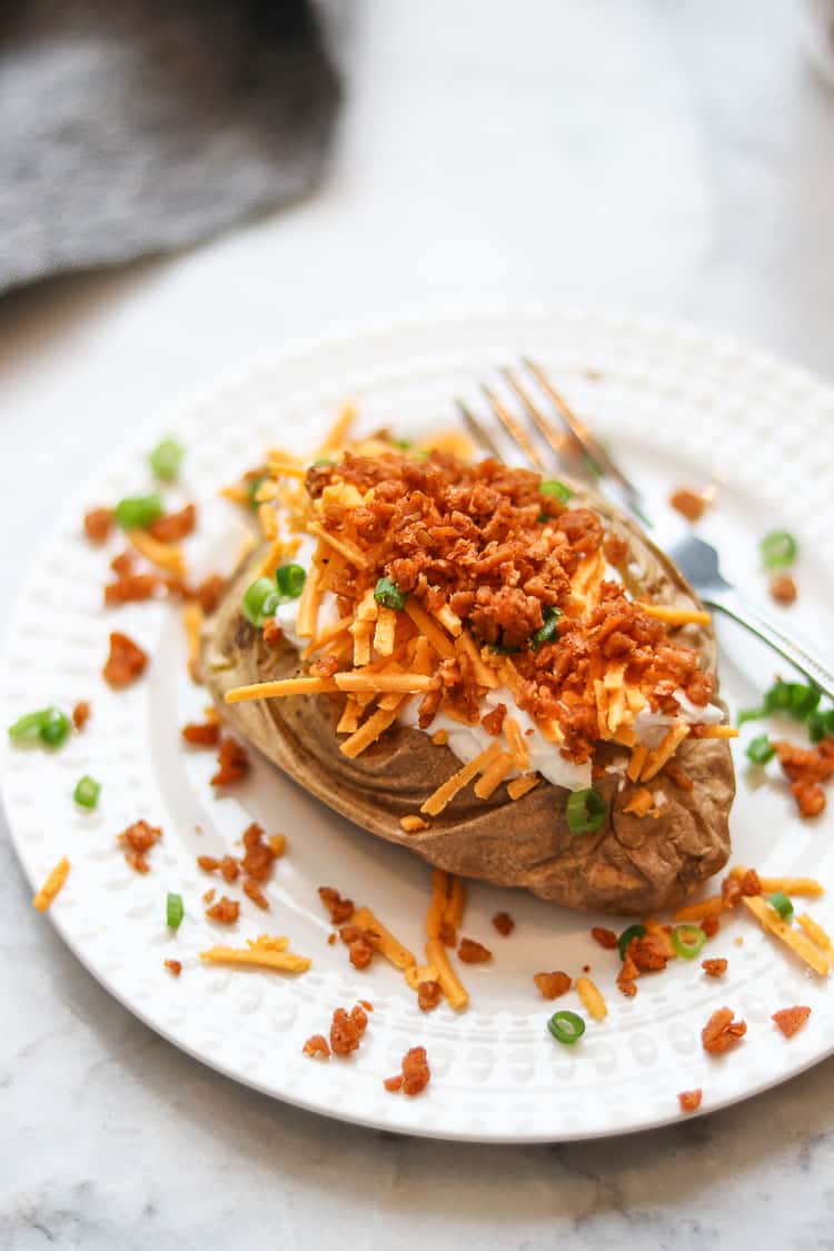 side overhead photo of a baked potato loaded with vegan sour cream, cheese, scallions, and bacon bits