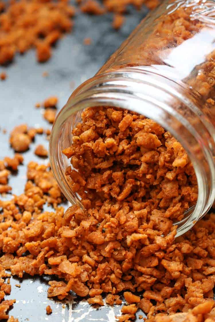 mini glass jar full of vegan bacon bits turned on its side on a black baking tray