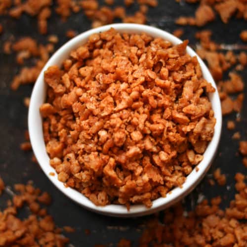 overhead closeup shot of vegan bacon bits in a white finger bowl setting on a black baking tray