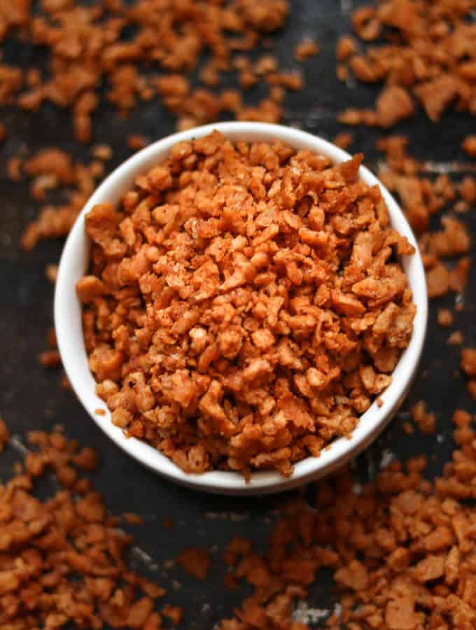 overhead closeup shot of vegan bacon bits in a white finger bowl setting on a black baking tray