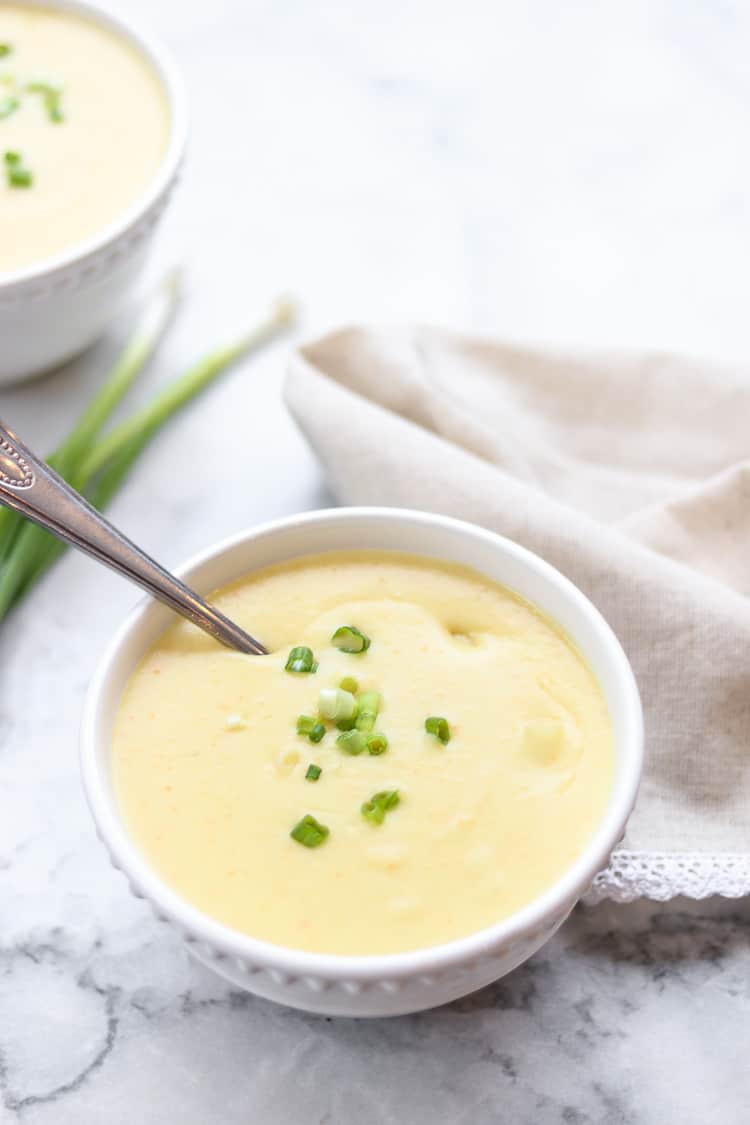 side overhead closeup shot of creamy vegan potato soup in a bowl with green scallions nearby