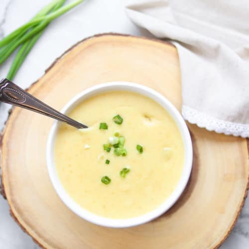 overhead shot of a bowl of creamy vegan potato soup with slices of scallions on a wood board background