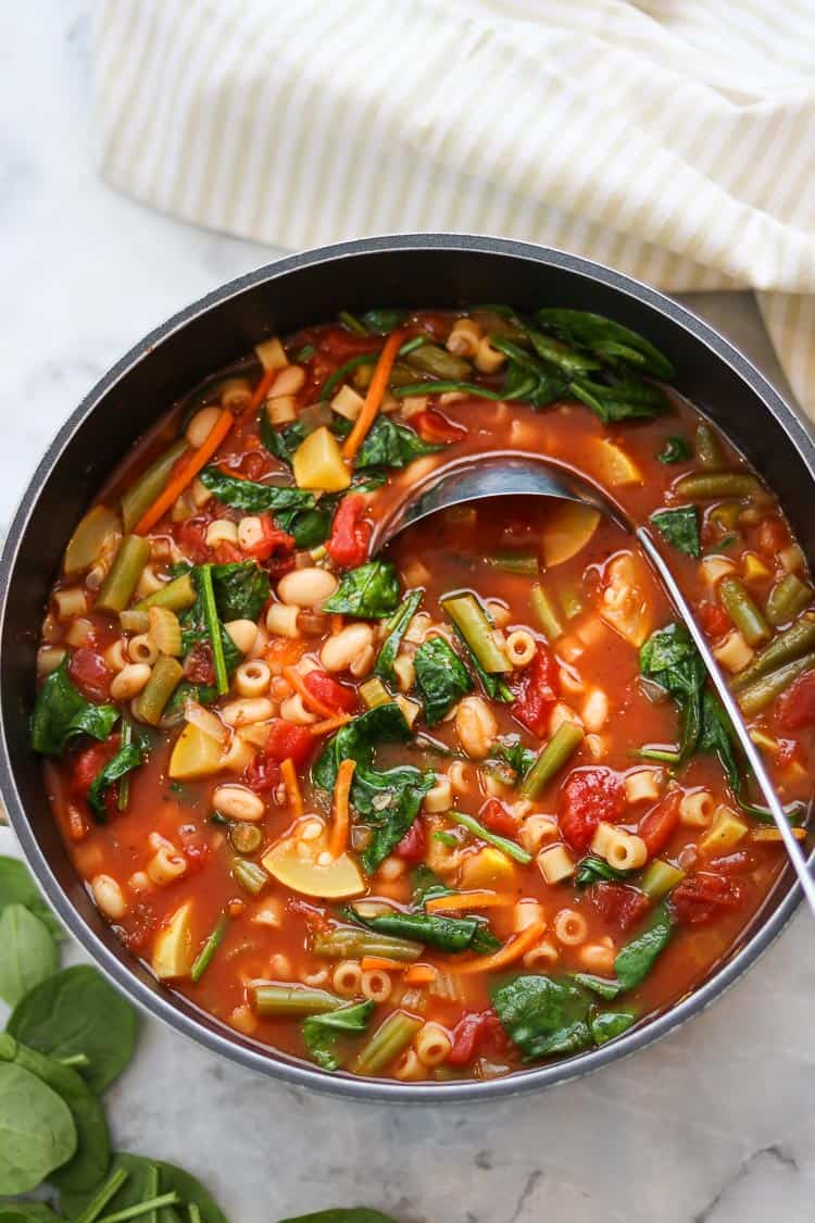 overhead photo of complete vegan minestrone in a large soup pot with silver ladle