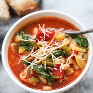 overhead photo of vegan minestrone in a white bowl with a sprinkle of vegan parmesan on top
