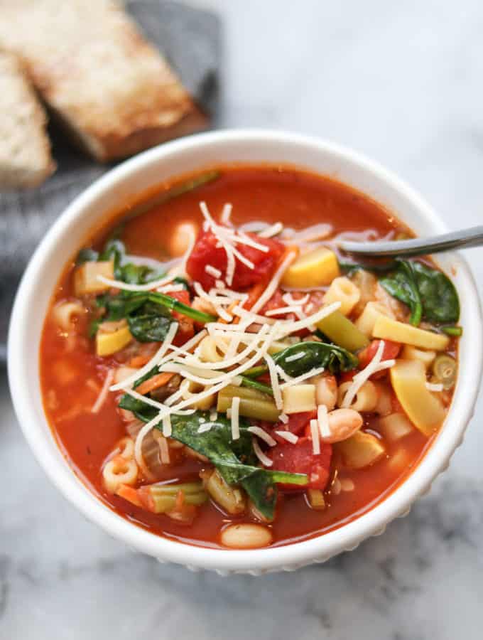 overhead photo of vegan minestrone in a white bowl with a sprinkle of vegan parmesan on top
