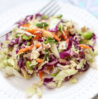 side overhead closeup shot of cabbage salad with ramen noodles on a white plate with fork and marble background