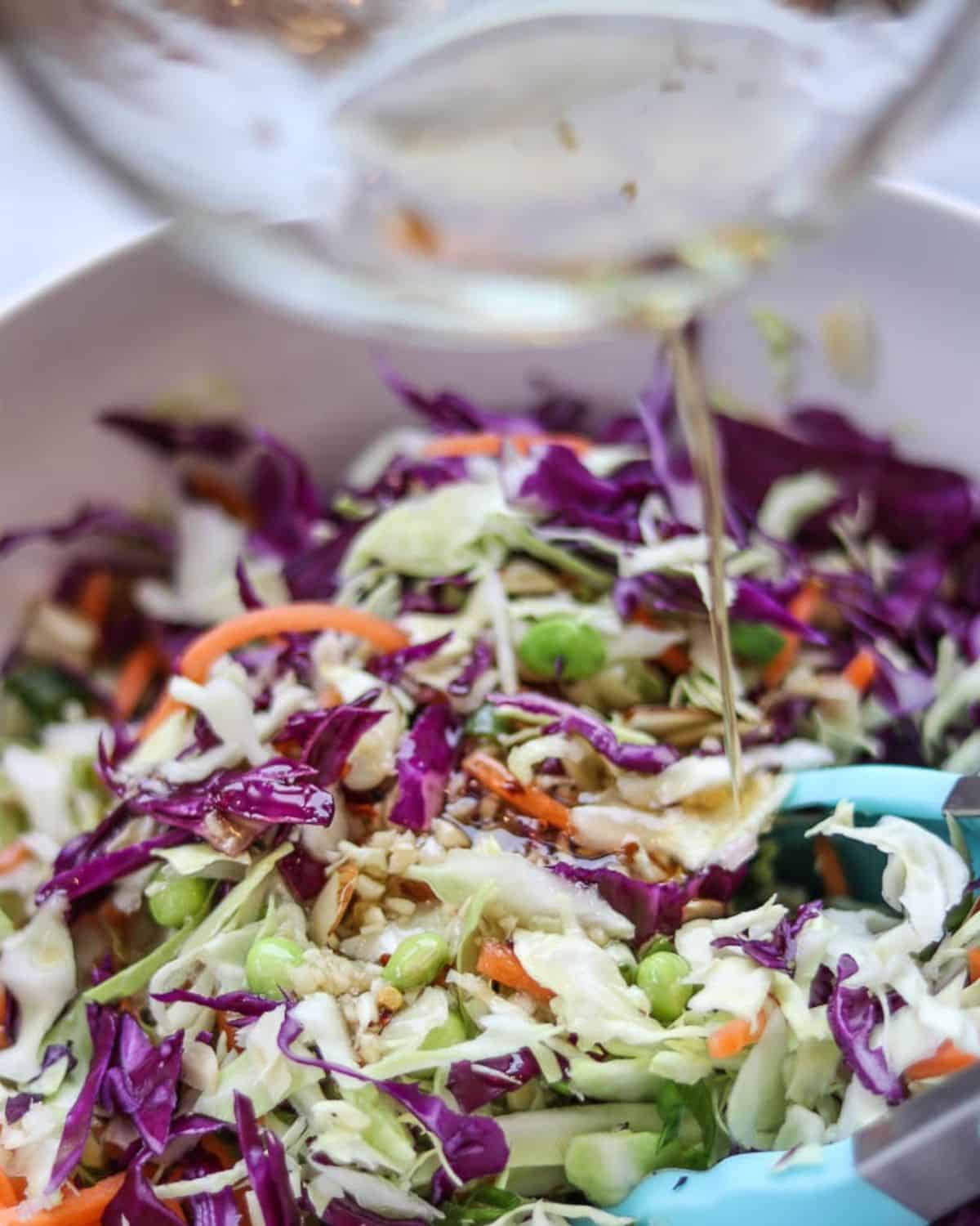 Adding asian dressing to cabbage ramen noodle salad.