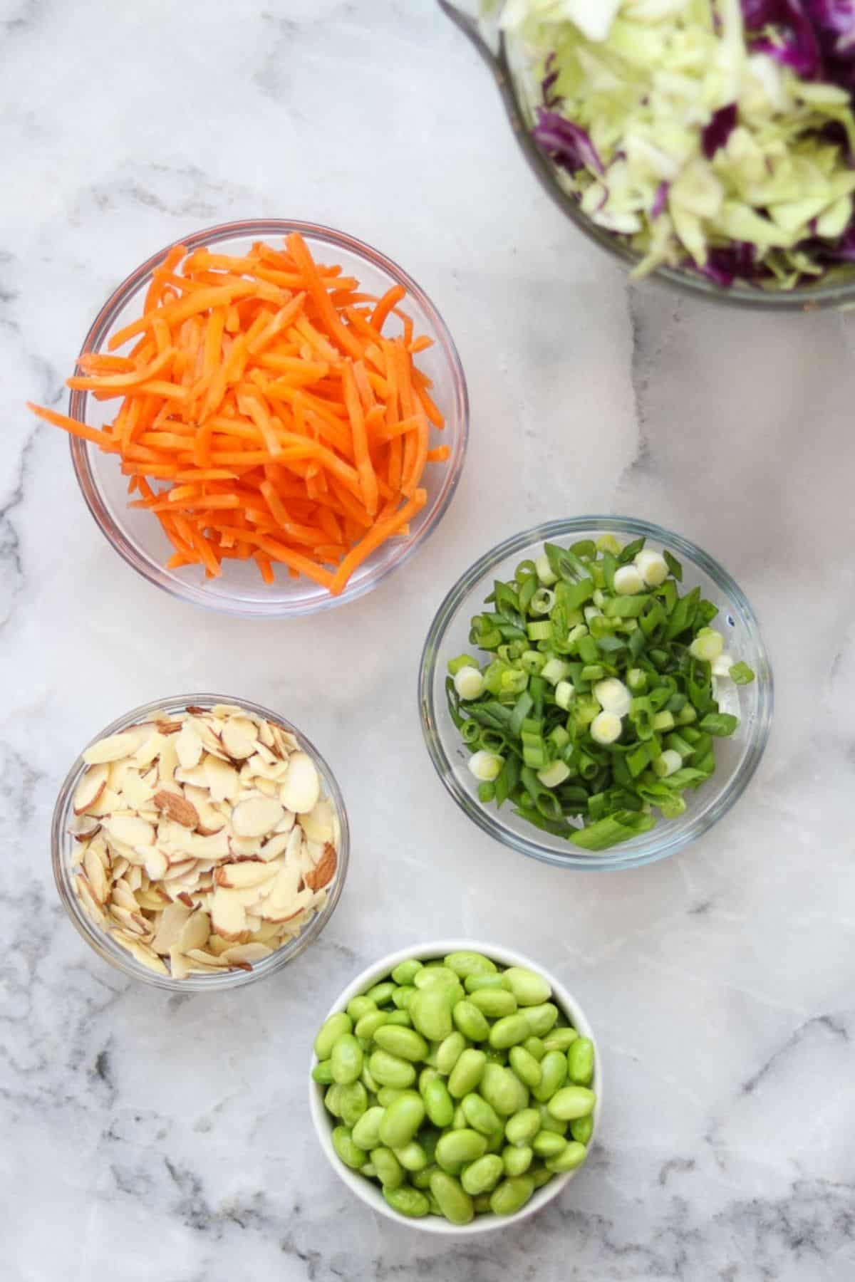 Grated carrots, chopped scallion, slivered almoonds, edamame, and chopped cabbage ingredients.