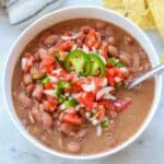overhead photo of pinto beans in a white bowl with tomatoes, onions and jalapeños on top
