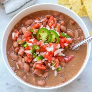 overhead photo of pinto beans in a white bowl with tomatoes, onions and jalapeños on top