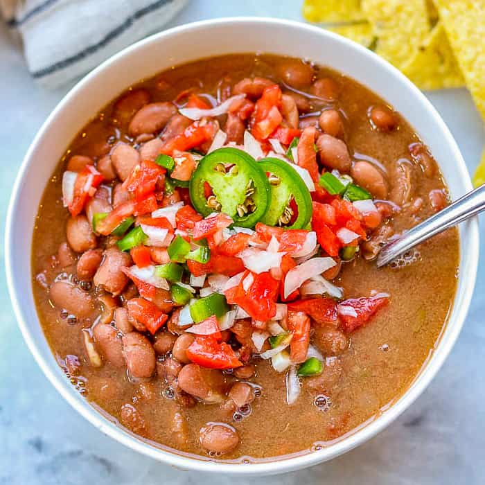 bowl of slow cooker pinto beans topped with salsa and sliced jalapenos