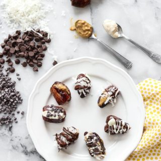 wide overhead photo of chocolate stuffed dates on a white plate with toppings all around