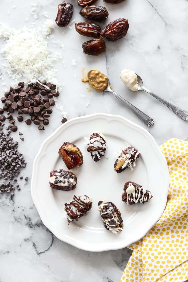 overhead photo of chocolate dates on a white plate with spoons of peanut butter and cream cheese nearby