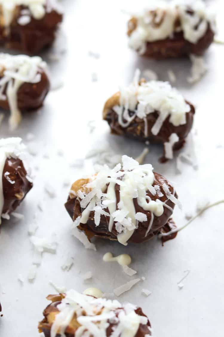 overhead photo of dates dipped in chocolate with peanut butter inside and coconut shreds on top lined up on a baking tray