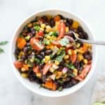 overhead closeup photo of a white bowl filled with bean, corn, tomato and pepper salad