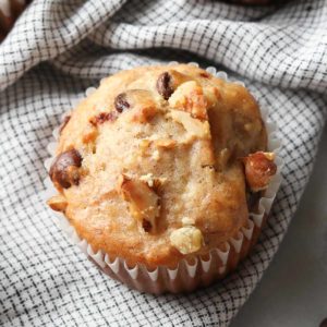 overhead photo of banana bread muffin on a checked napkin with chocolate chips and chopped walnuts