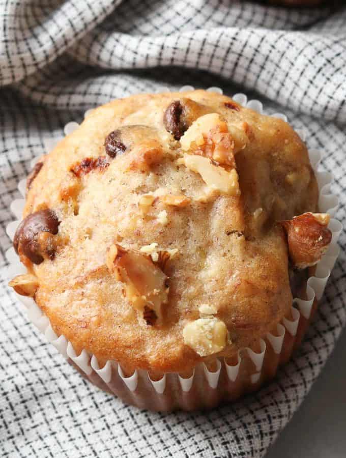 overhead photo of banana bread muffin on a checked napkin with chocolate chips and chopped walnuts