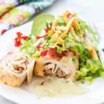 side overhead photo of sliced chimichanga on a white plate loaded with toppings including shredded cheese, lettuce, avocado, nacho cheese sauce, pico de gallo