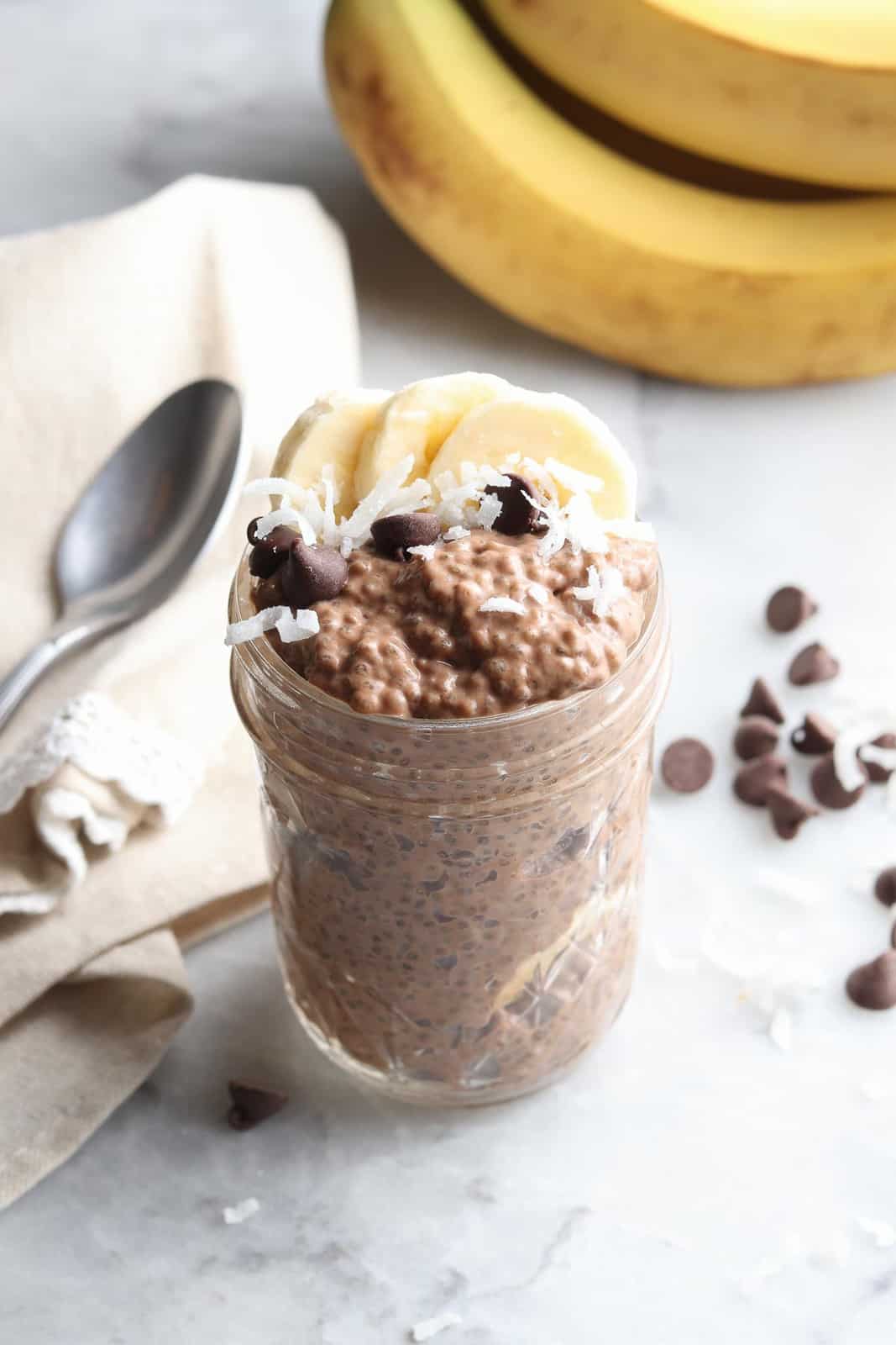 chocolate chia pudding in a pint-sized mason jar topped with banana slices, chocolate chips, and shredded coconut
