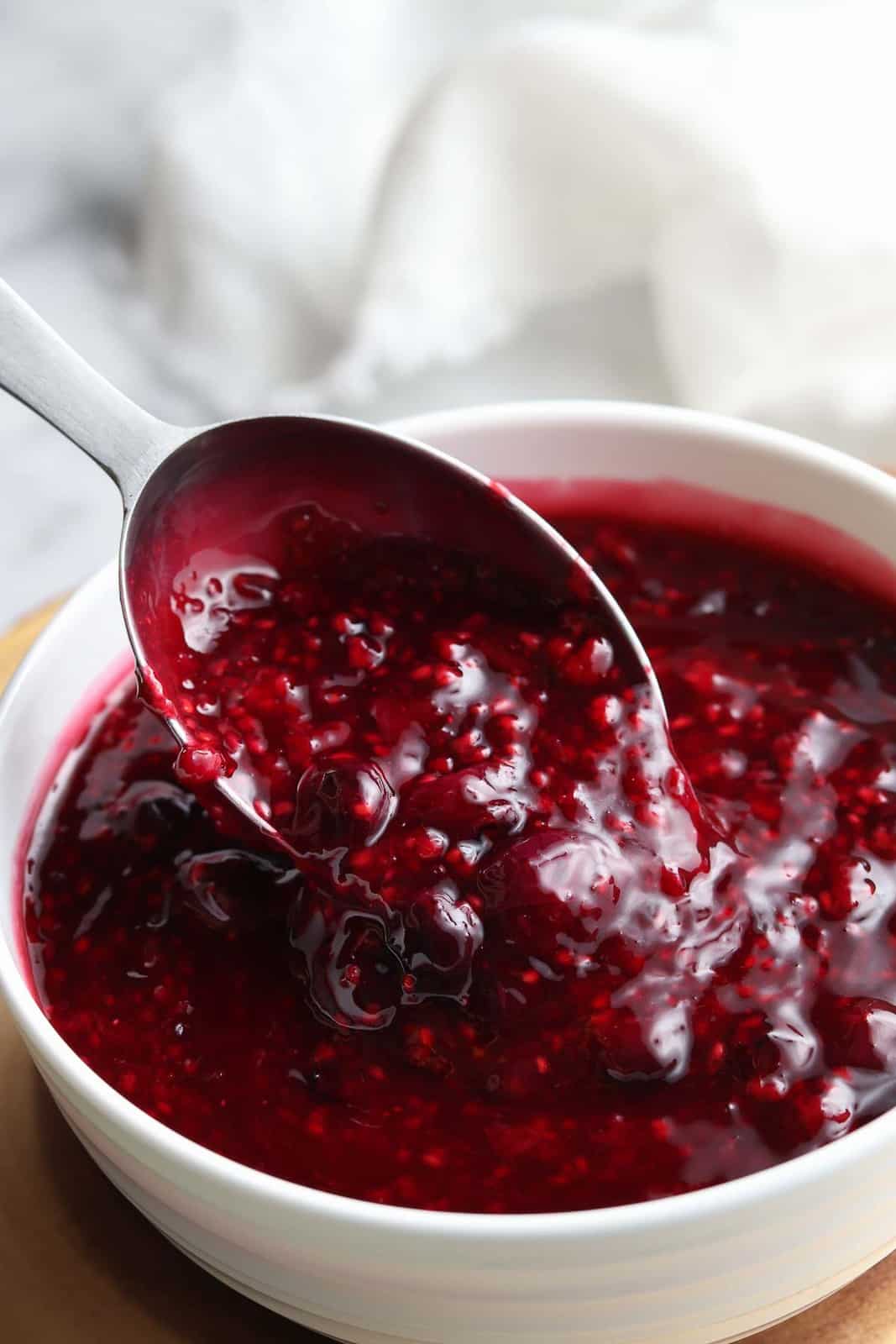 overhead photo of silver serving spoon lifting berry sauce out of white bowl