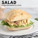 vegan chicken salad sandwich on a white plate with folded checked napkin beneath and toothpicks in the background with text overlay for pinterest