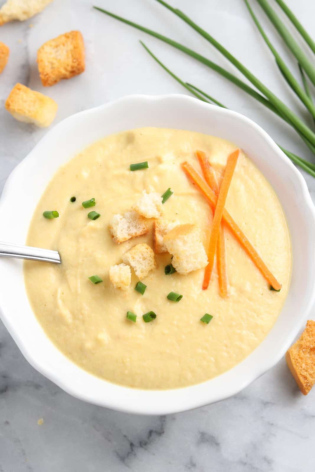 closeup overhead shot of creamed soup in a white bowl with chopped green chives, croutons, and shredded carrot sticks as garnish