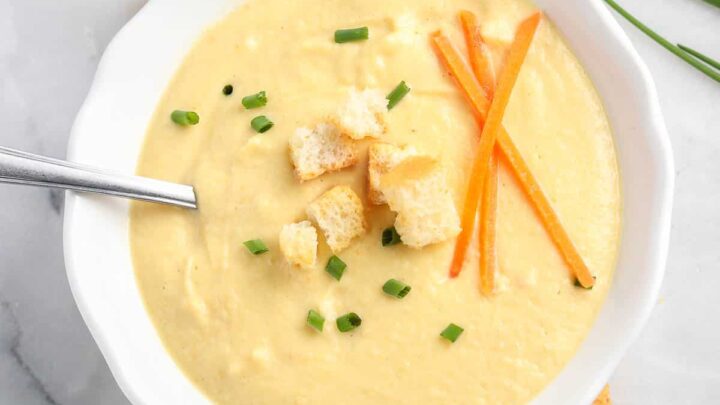 overhead photo of creamy soup in a white bowl garnished with broken croutons, carrot sticks, and chopped chives