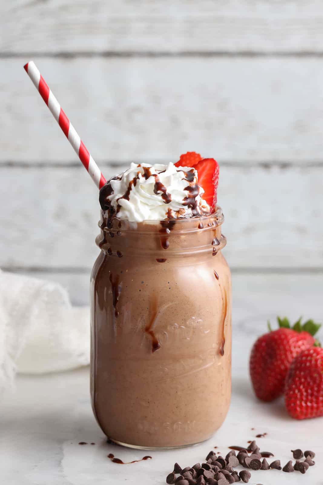 side view of milkshake in a pint jar with chocolate syrup dripping down the sides and a straw sticking out of the top setting on a marble countertop
