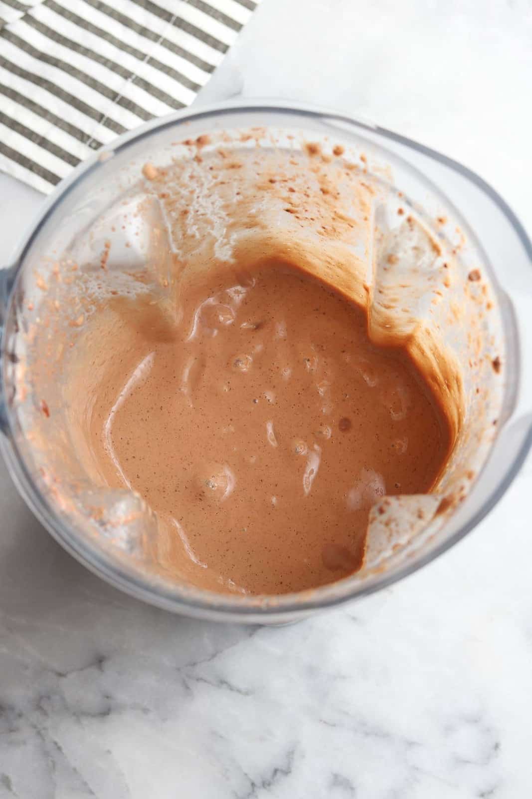 overhead view looking down into blender showing smooth pureed chocolate shake, with striped napkin in the background