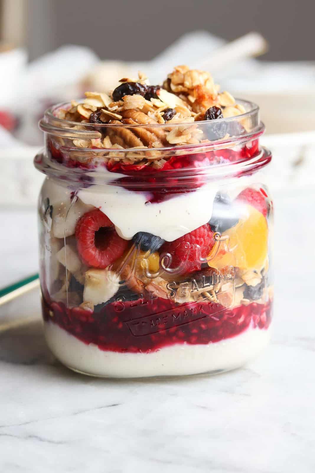 side overhead photo showing layers of yogurt, fruit sauce, fruit, and granola in a pint-sized jar