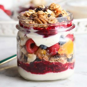 side overhead closeup photo of layered vegan yogurt parfait with berries, peaches, and granola