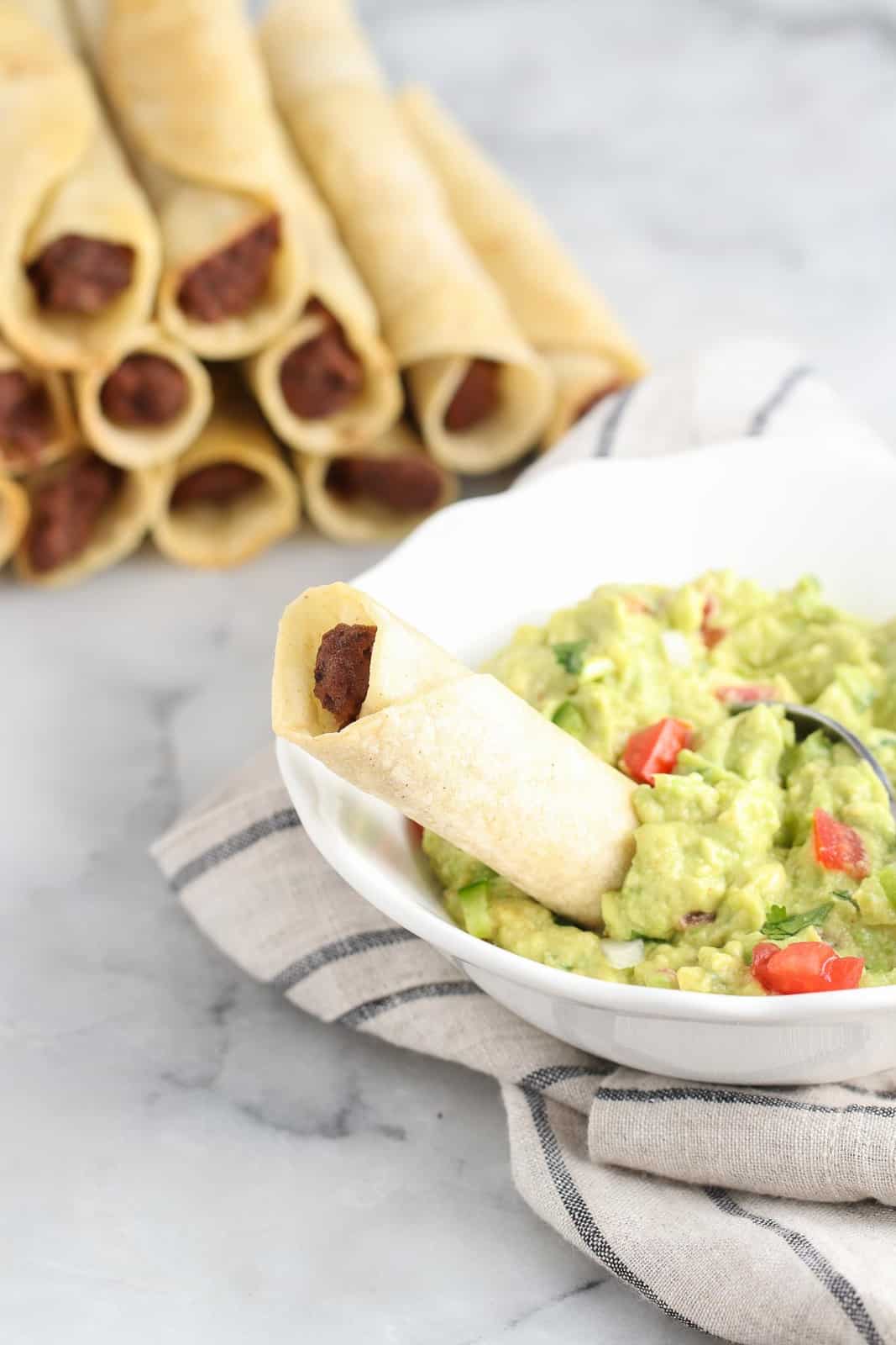 overhead shot showing rolled corn taquito being dipped into guacamole bowl