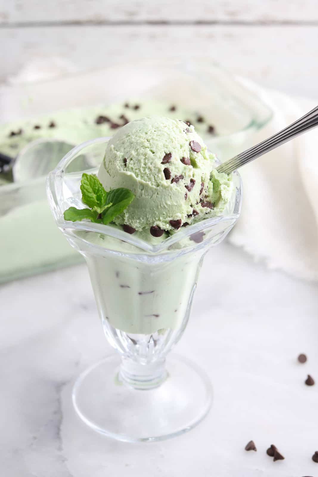 vegan mint chip ice cream in a clear ice cream glass with sprig of mint for garnish