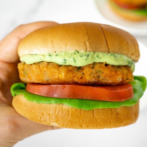 hand holding lentil burger topped with creamy vegan avocado sauce