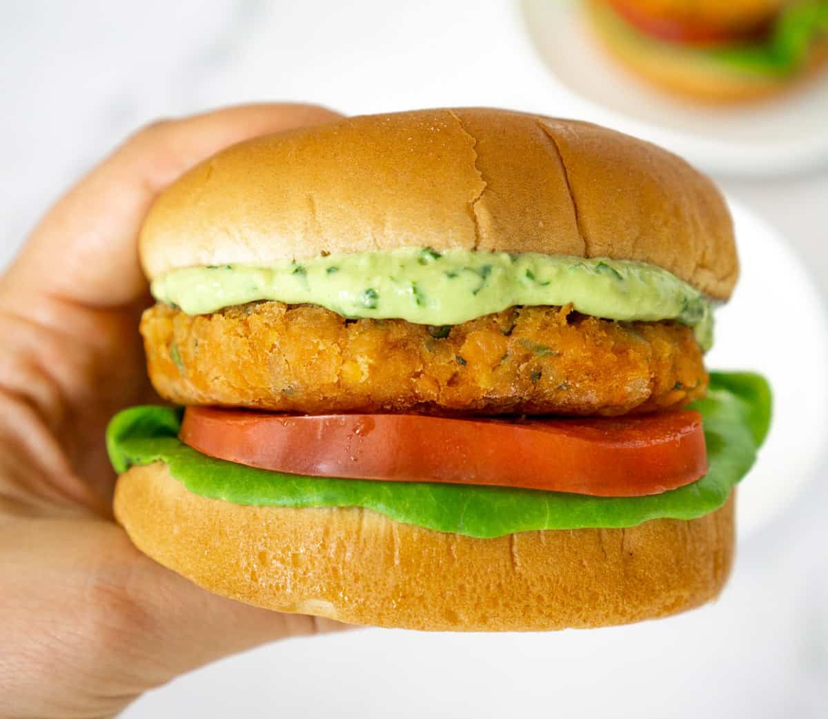 hand holding lentil burger topped with creamy vegan avocado sauce